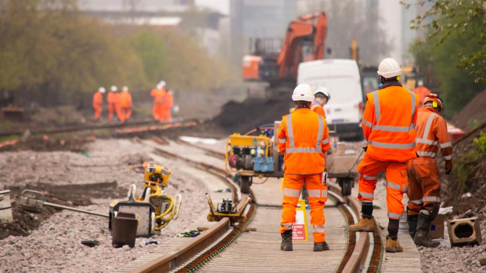 Männer in orangen Arbeitsanzügen bei Gleisbauarbeiten