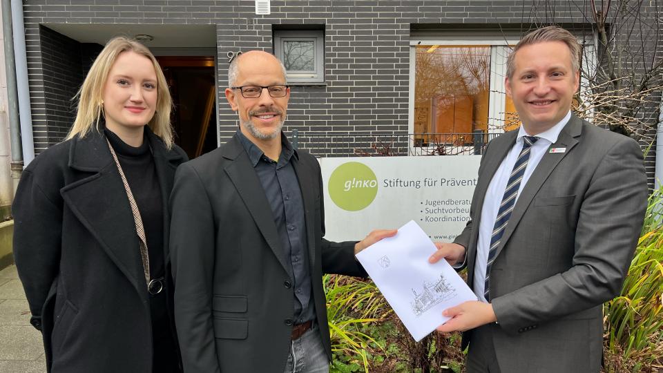 Regierungspräsident Thomas Schürmann (r.) übergab dem Leiter der Landesfachstelle Prävention, Armin Koeppe, den von Melina Mostert (l.) erstellten Förderbescheid über rund 2,2 Millionen Euro.