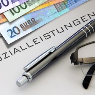 Stift und Geld mit dem Schriftzug "Sozialleistungen" (Symbolbild)