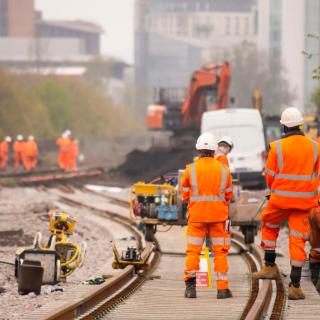 Männer in orangen Arbeitsanzügen bei Gleisbauarbeiten