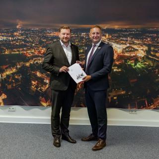 Regierungspräsident Thomas Schürmann (rechts) übergibt den Förderbescheid an Oberbürgermeister Tim Kurzbach.